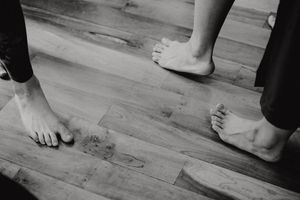 Black and white shot of bare feet on wooden dance floor during movement.