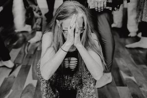 A black and white image showing a person in sparkly attire covering their face with their hands on a dance floor.