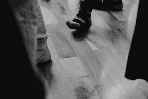 Close up view of feet and shoes on a hardwood floor in black and white.