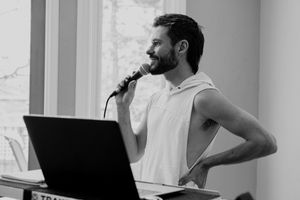 Performer sings into a microphone while playing electronic keyboard in black and white.