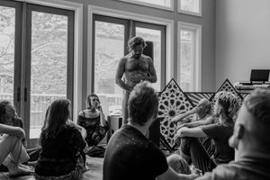 Live performance in front of attentive audience members in a sunny room with decorative railings.