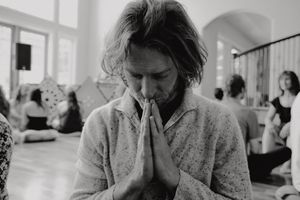 Person in a sweater meditating with hands clasped in prayer position during a group session.