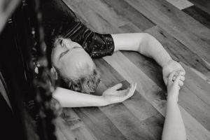 Person lying on wooden floor during expressive movement session captured in black and white.