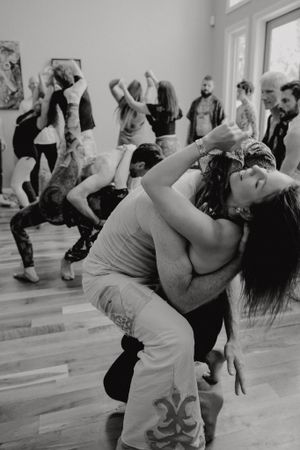Black and white photo of dancers performing in a studio with others visible in the background.