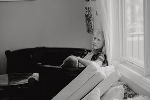 Black and white photo of person resting contemplatively by a bright window.