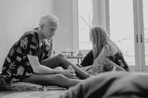 Two people sit on a wooden floor near a window having an intimate conversation in black and white.