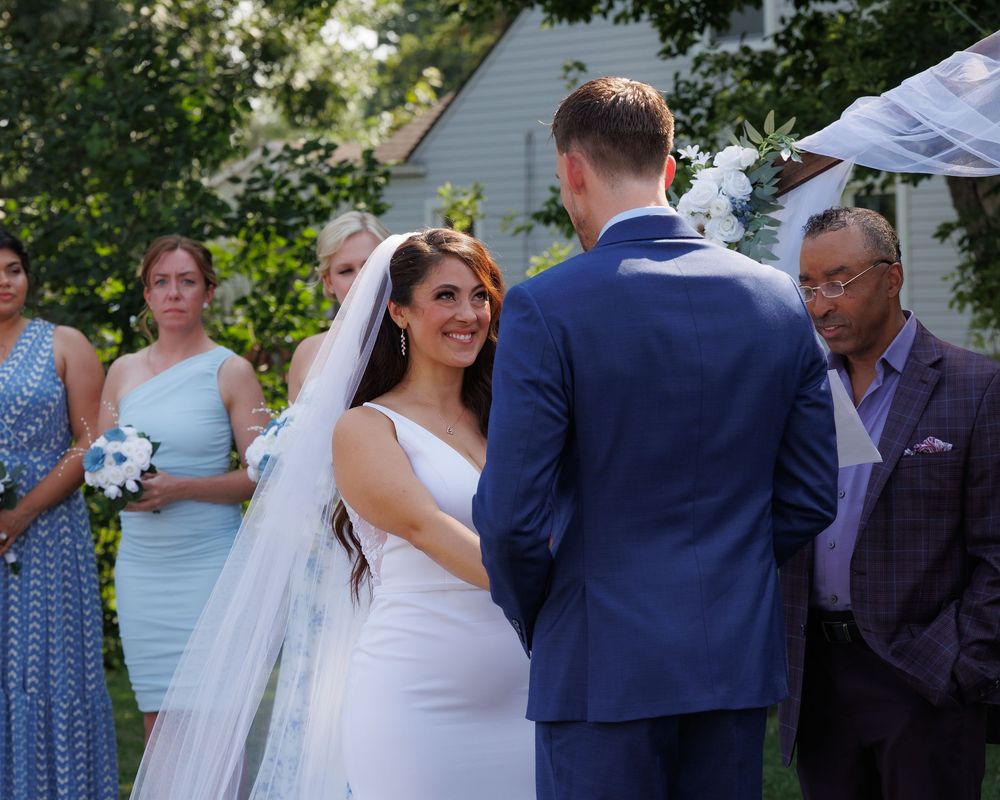 A couple exchanges vows during an outdoor garden wedding ceremony with guests looking on.