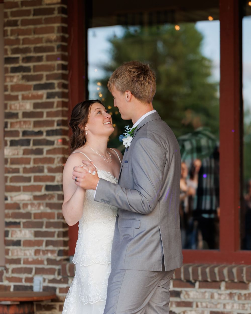 A couple shares their first kiss as newlyweds during an outdoor ceremony in front of a brick building.