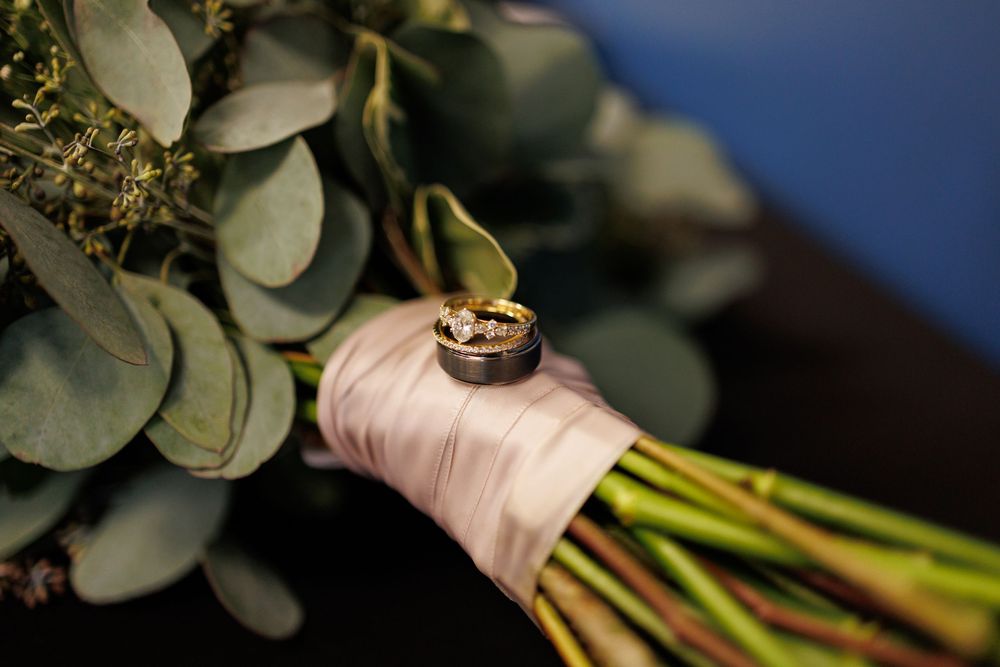 Two gold wedding rings resting on a pink satin ribbon wrapped around a bridal bouquet with eucalyptus greenery.