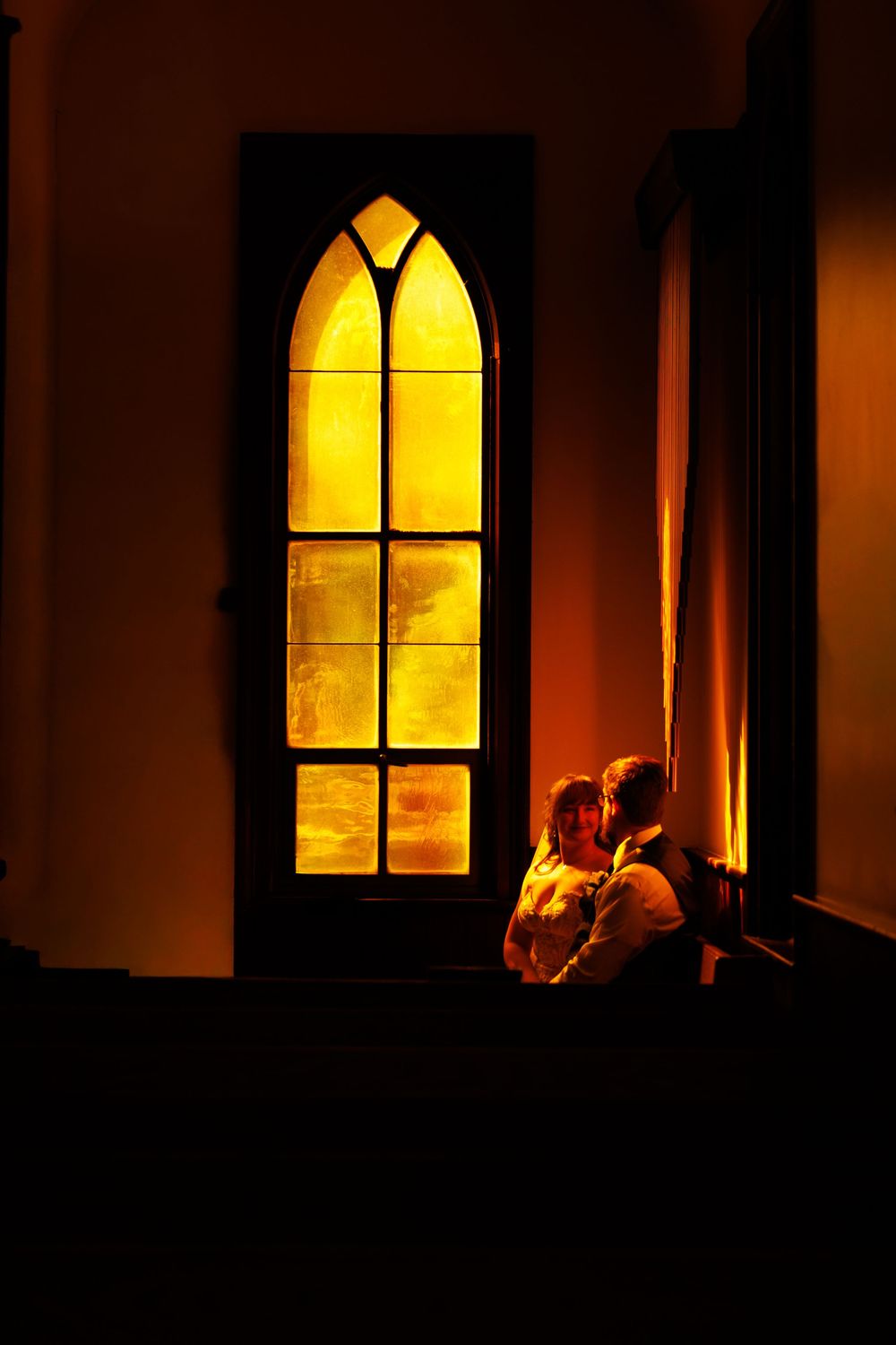 A sequence of gothic church windows glowing with warm yellow light against a dark background creates a dramatic silhouette.