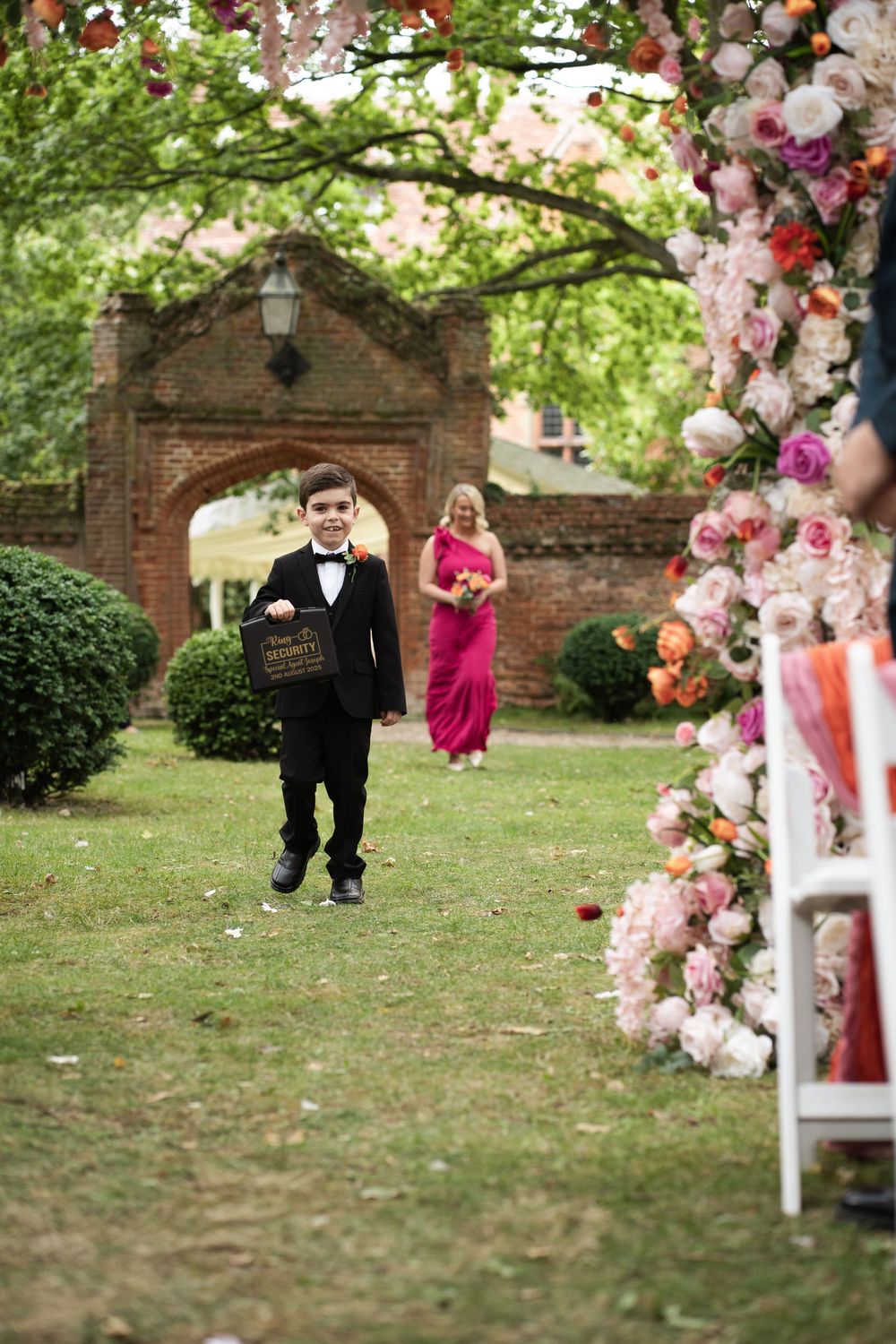 Decorative garden wedding ceremony setup with pink and white floral arrangements framing a walkway through green grass.
