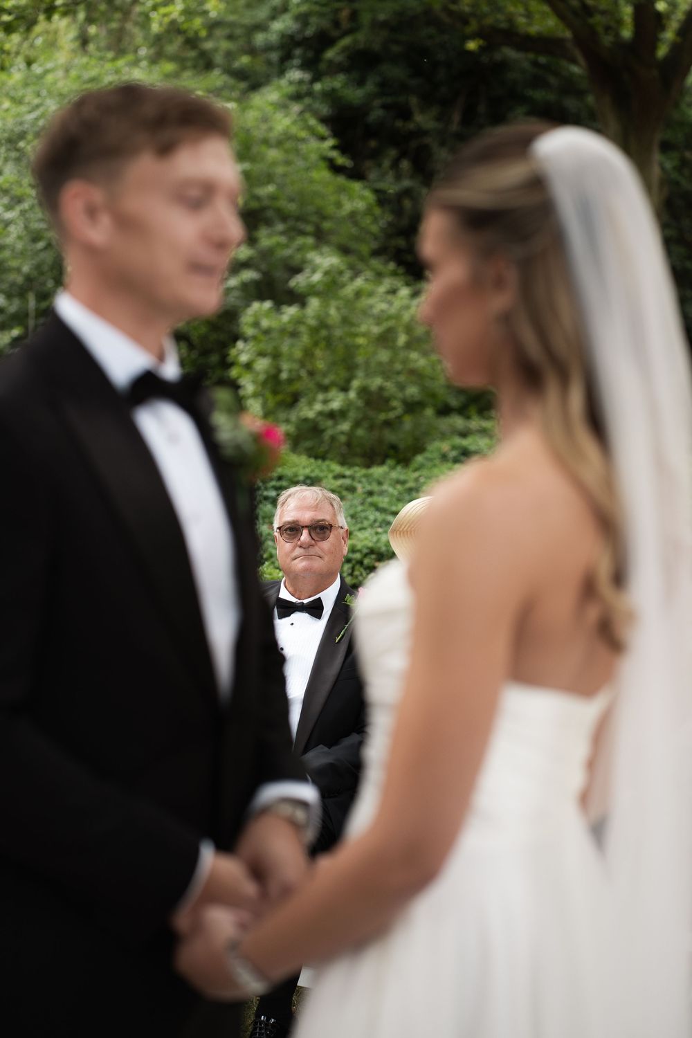 A couple stands at the altar during their outdoor wedding ceremony with an officiant in sunglasses visible between them.