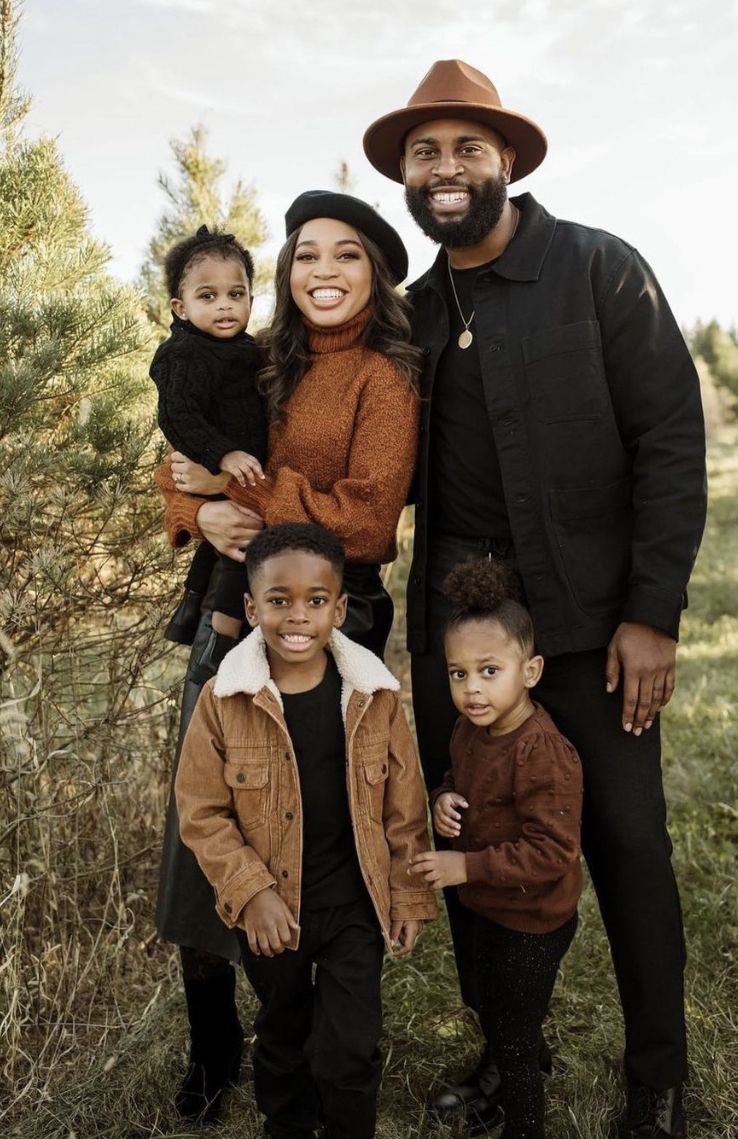 A family poses together outdoors wearing coordinated brown and black outfits for a fall portrait session.