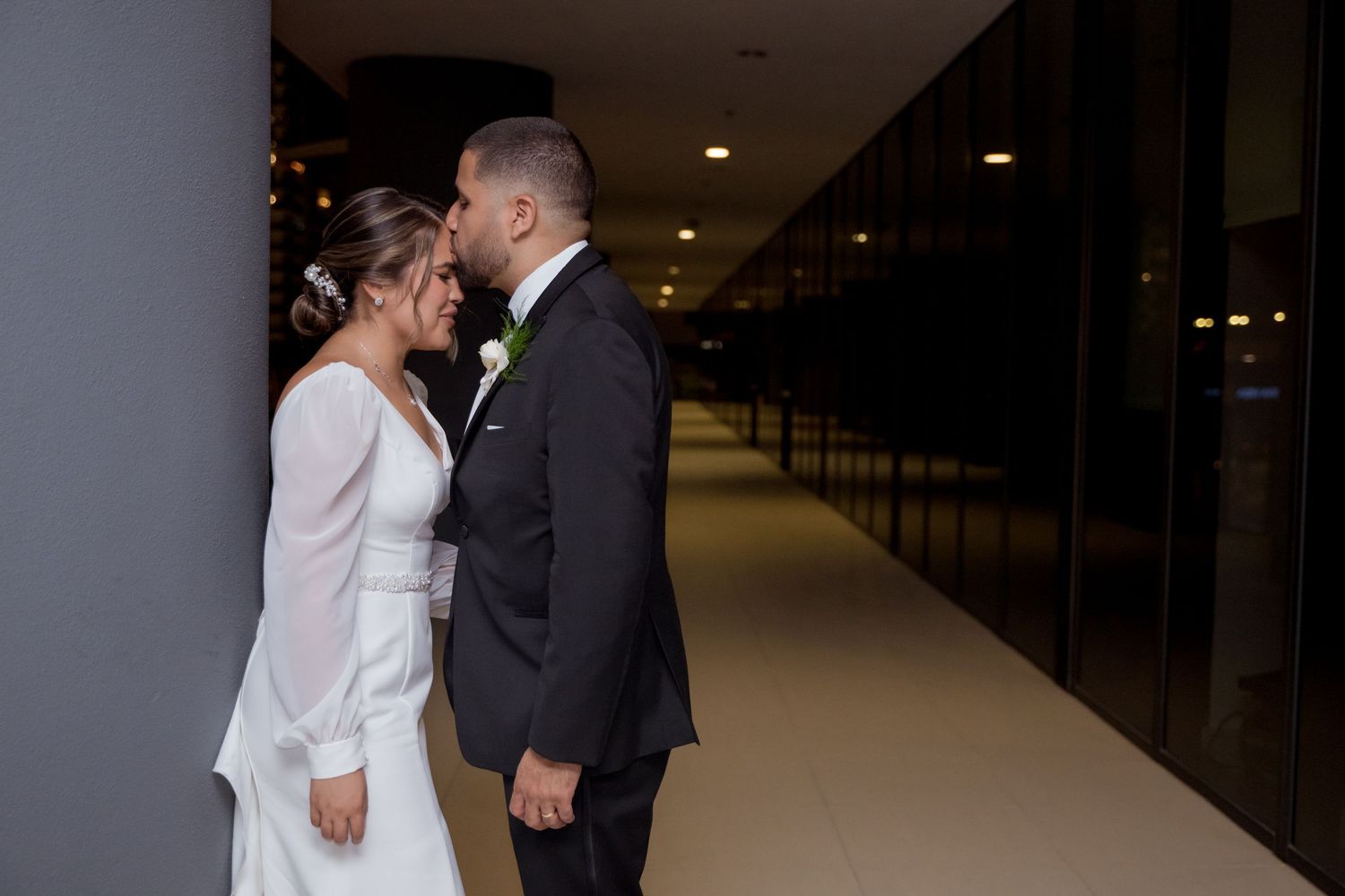A couple shares an intimate moment together in a long hallway wearing formal wedding attire.