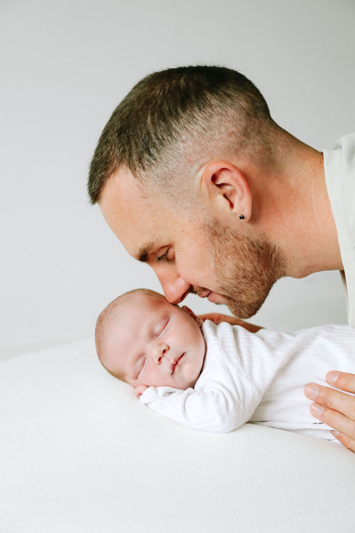 A tender moment captured between a parent and sleeping newborn baby against a white background, during newborn shoot based in Nottingham