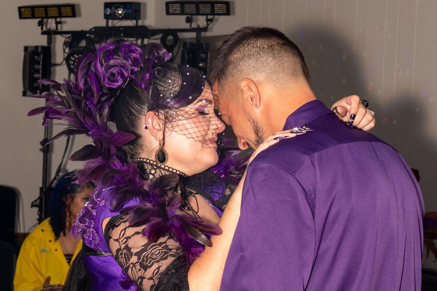 A group of people wearing purple feather boas dance together at a party or celebration event.