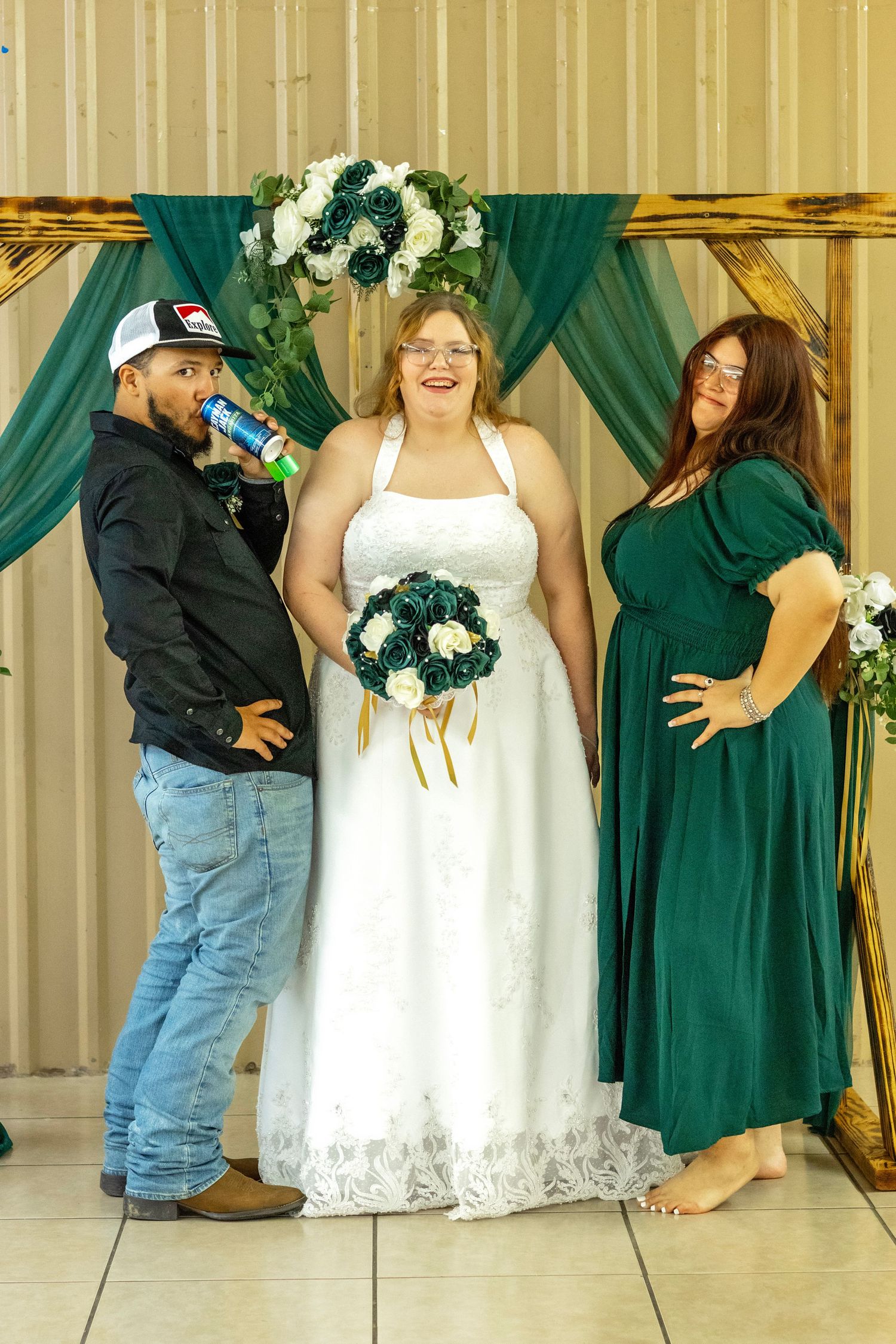 Bridal party members in emerald green dresses and white gown stand together against a light backdrop.