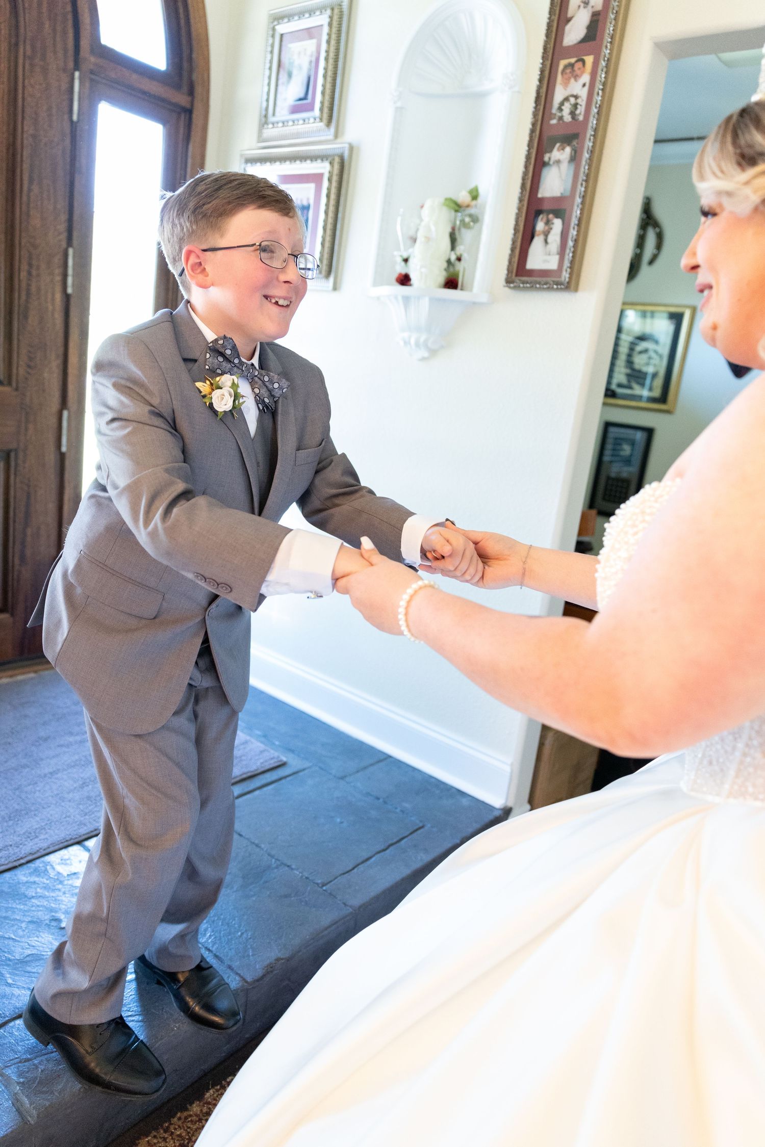 Young boy in gray suit holding hands with bride in white dress during wedding ceremony indoors.