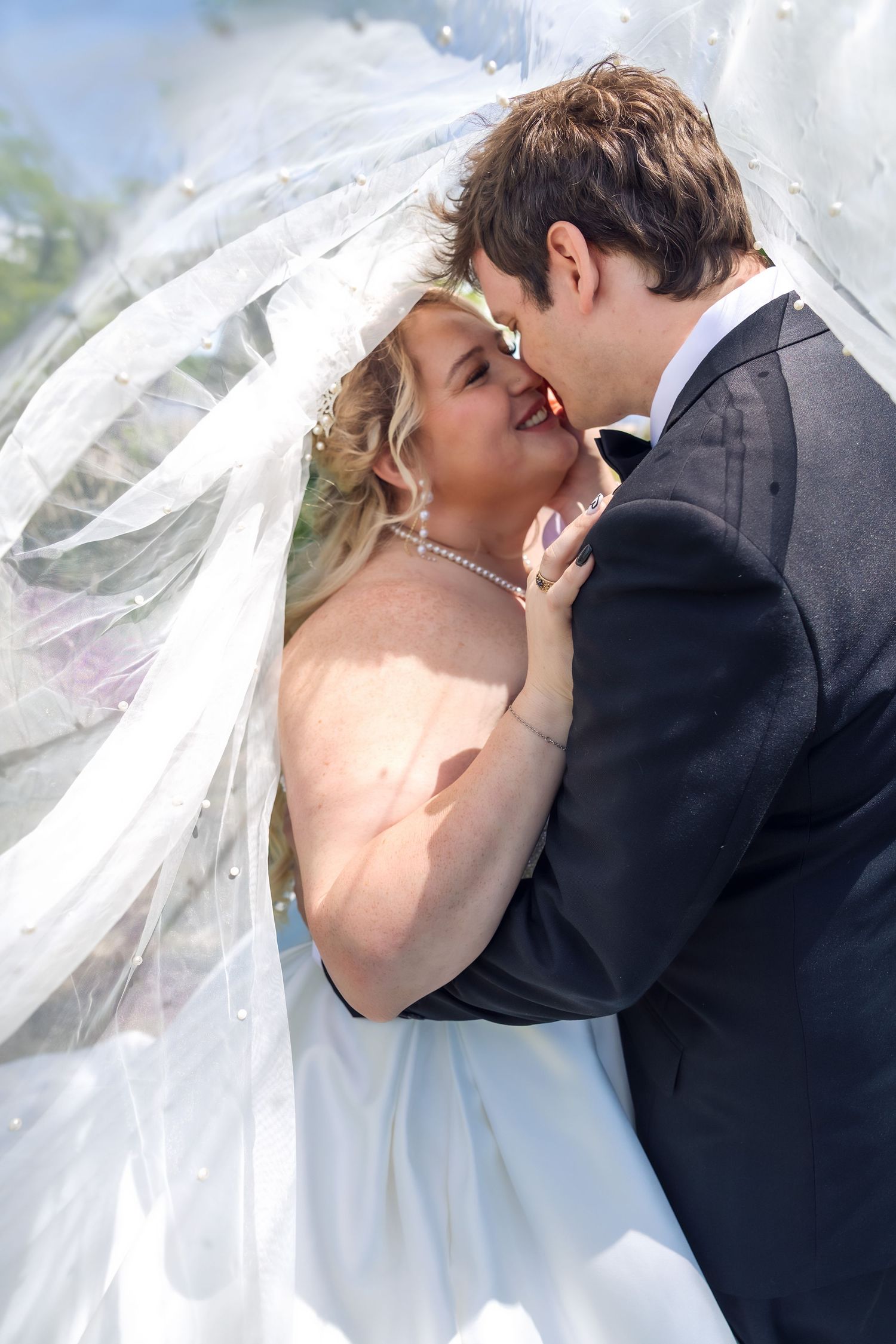 Bride and groom sharing a romantic moment under a flowing white veil on their wedding day.