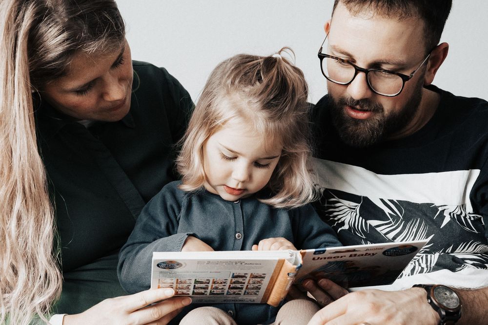 Junges Familienglück. Eltern schauen mit Tochter ein Bilderbuch an