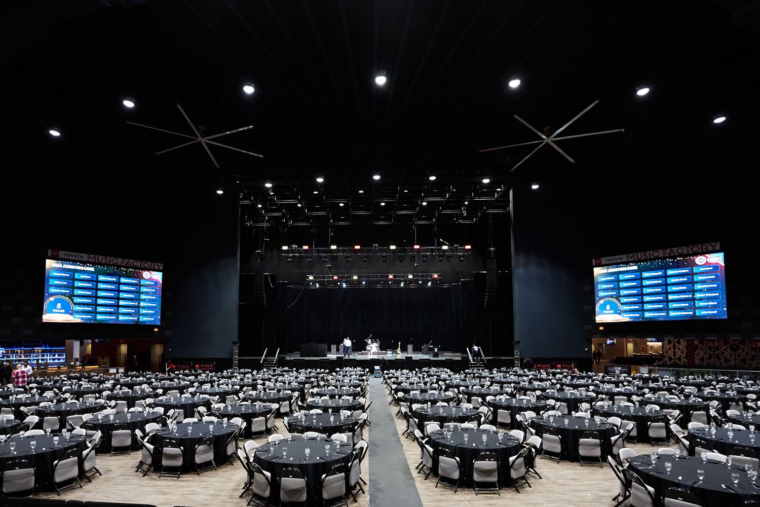 Panoramic view of a large conference venue with round tables and a dark atmosphere lit by overhead lighting and digital screens.