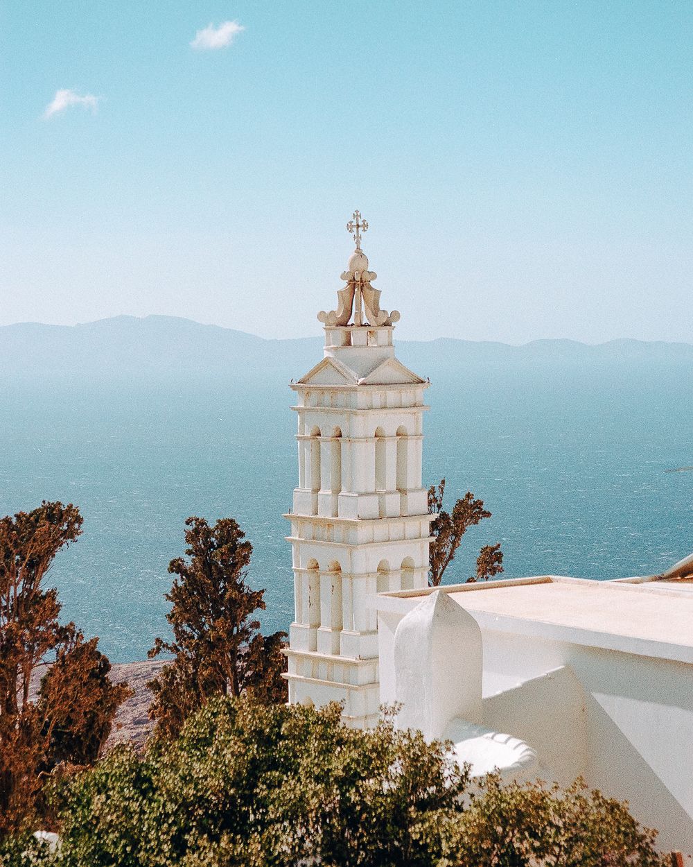 Bell tower rising above whitewashed buildings with sea in the distance