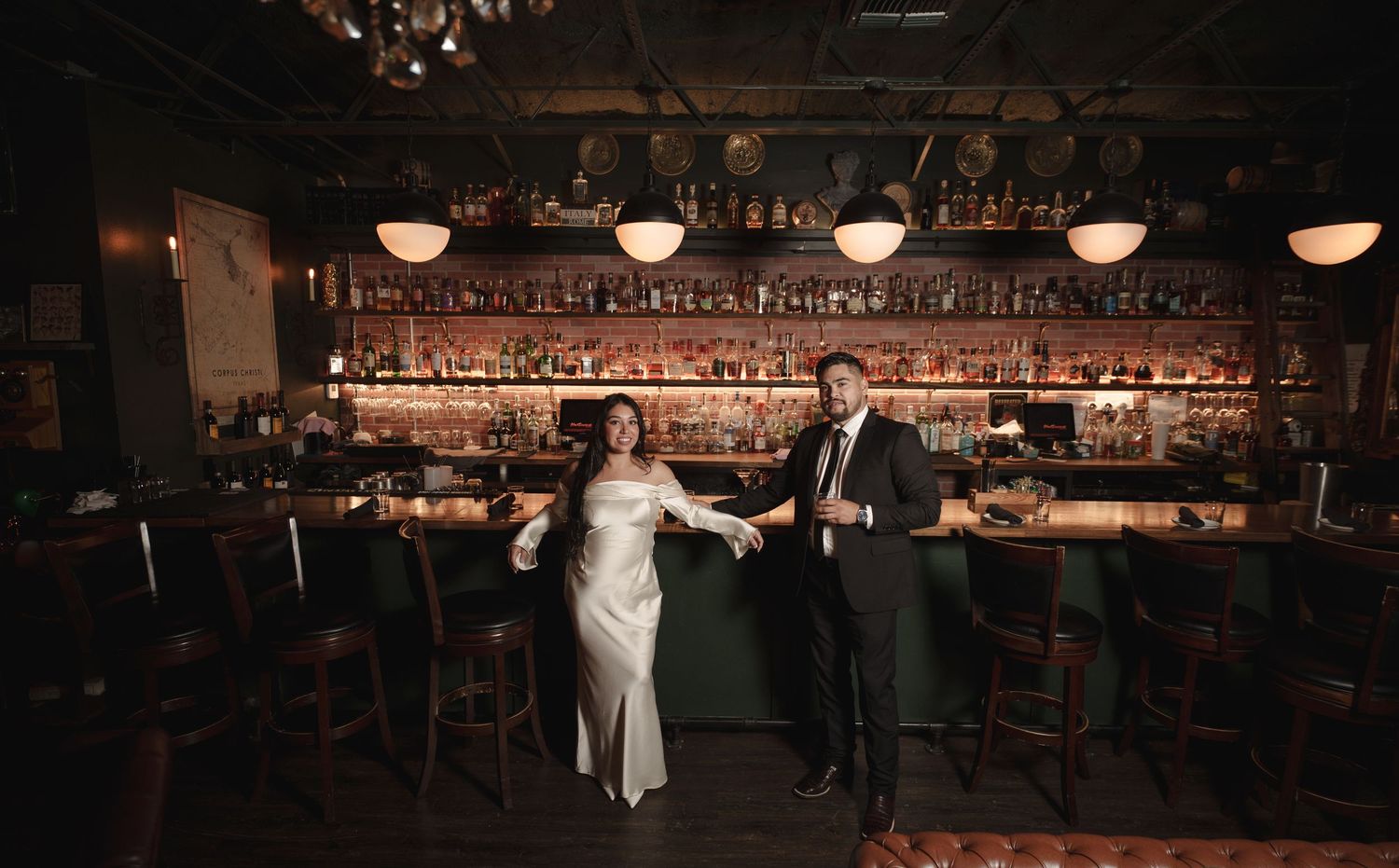 A couple dances intimately in a dimly lit bar with vintage decor and glowing pendant lights overhead.