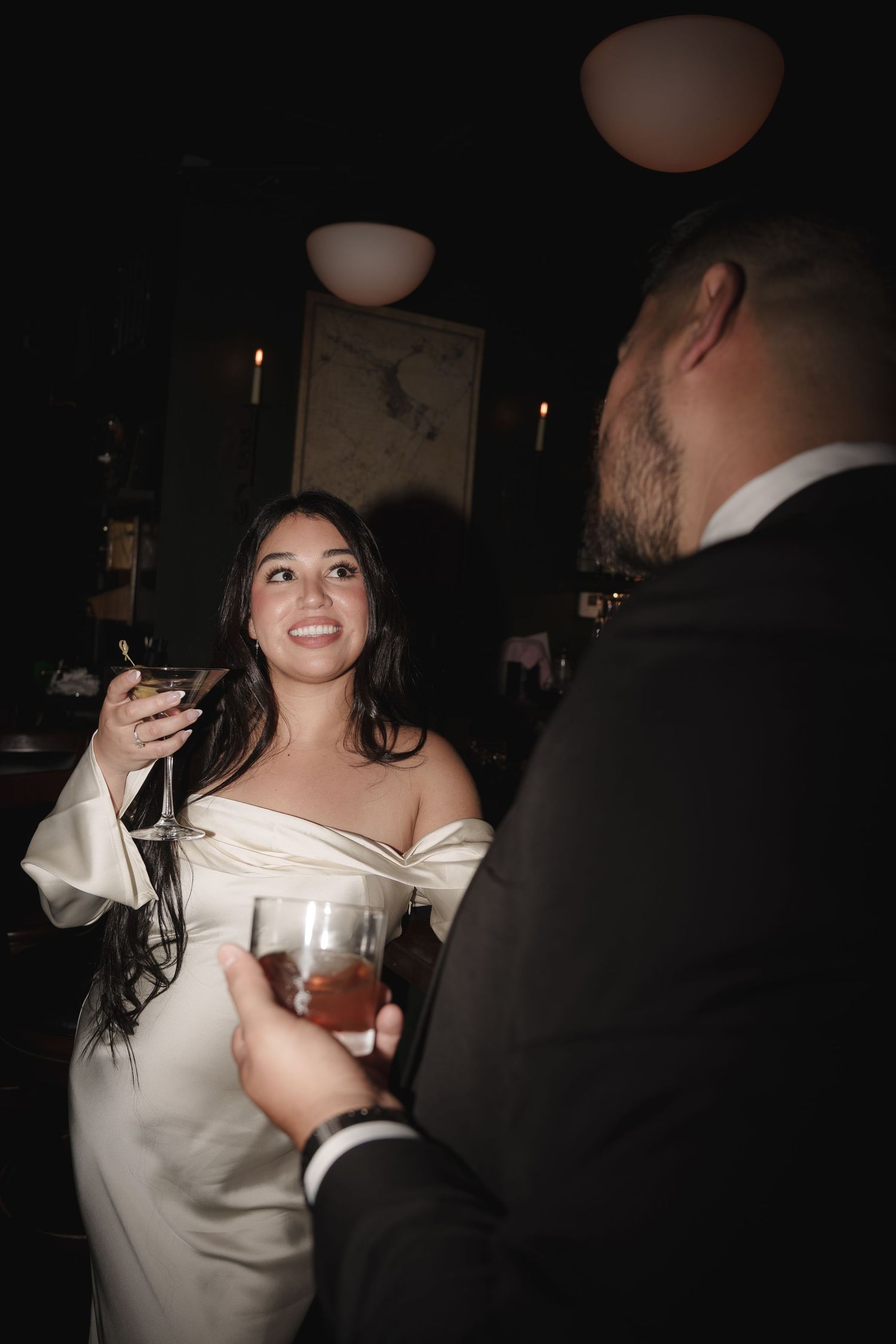 A couple enjoys drinks and laughter in an atmospheric bar setting.