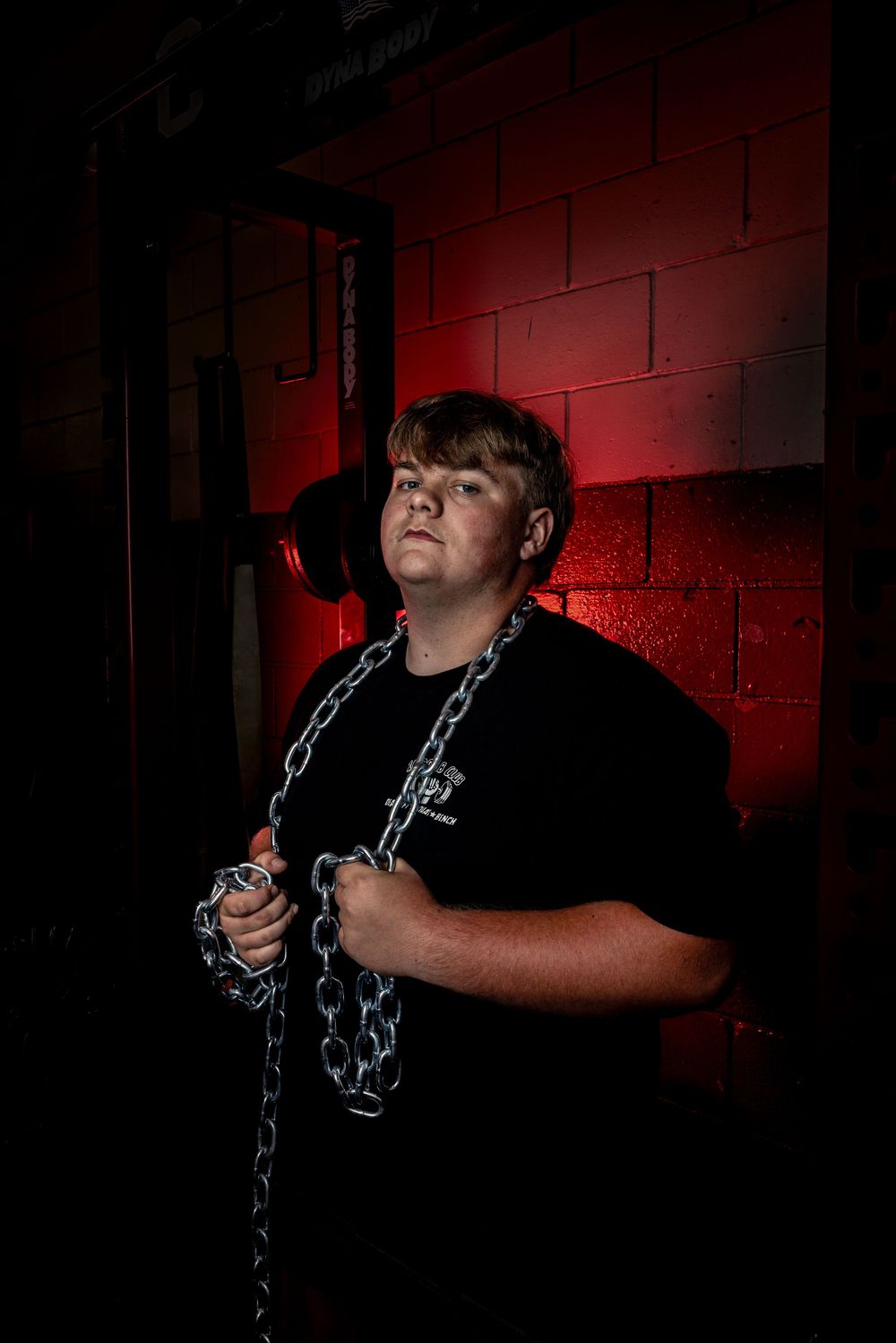 Dramatic portrait of someone holding chains against a dark wall with red lighting.