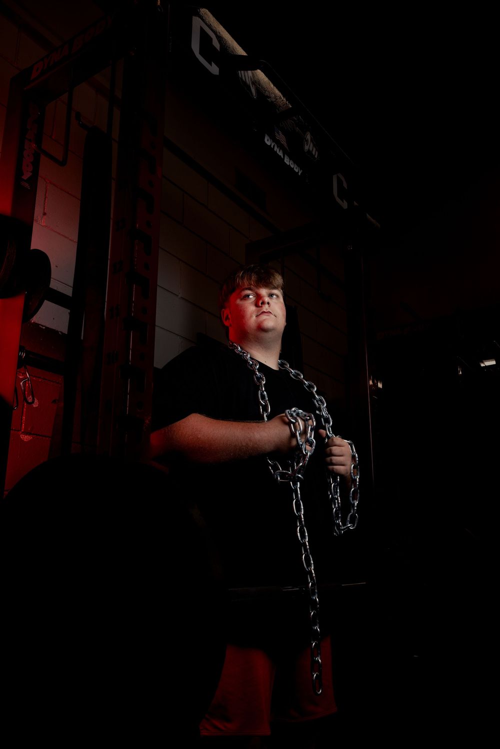 A person holding chains in a dimly lit room with red accent lighting.