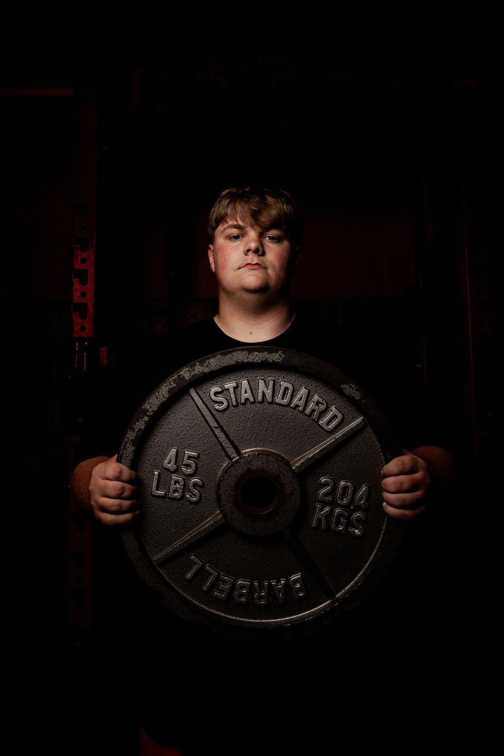 Person holding up large 45 pound standard weight plate against dark background in moody lighting.