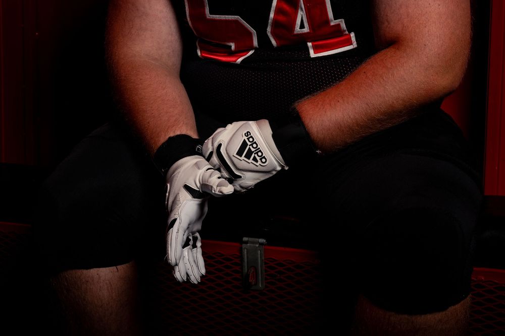 Close-up of athletic gloved hands against dark background with number 54 jersey visible.