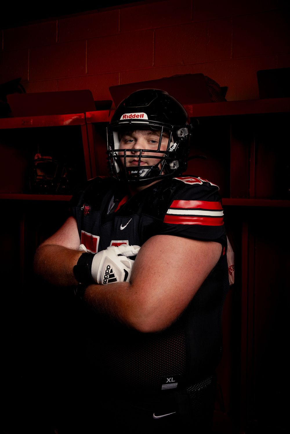 Football player poses in dark locker room wearing black helmet and Nike uniform with red lighting effects.