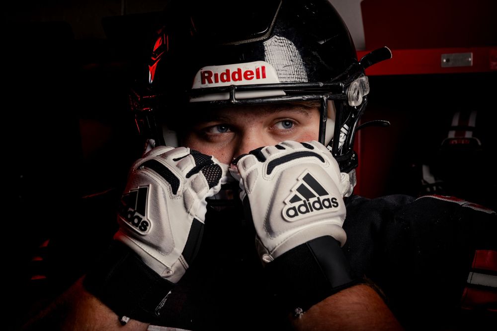 Close up sports portrait of someone wearing a Riddell helmet and Adidas batting gloves in moody lighting.