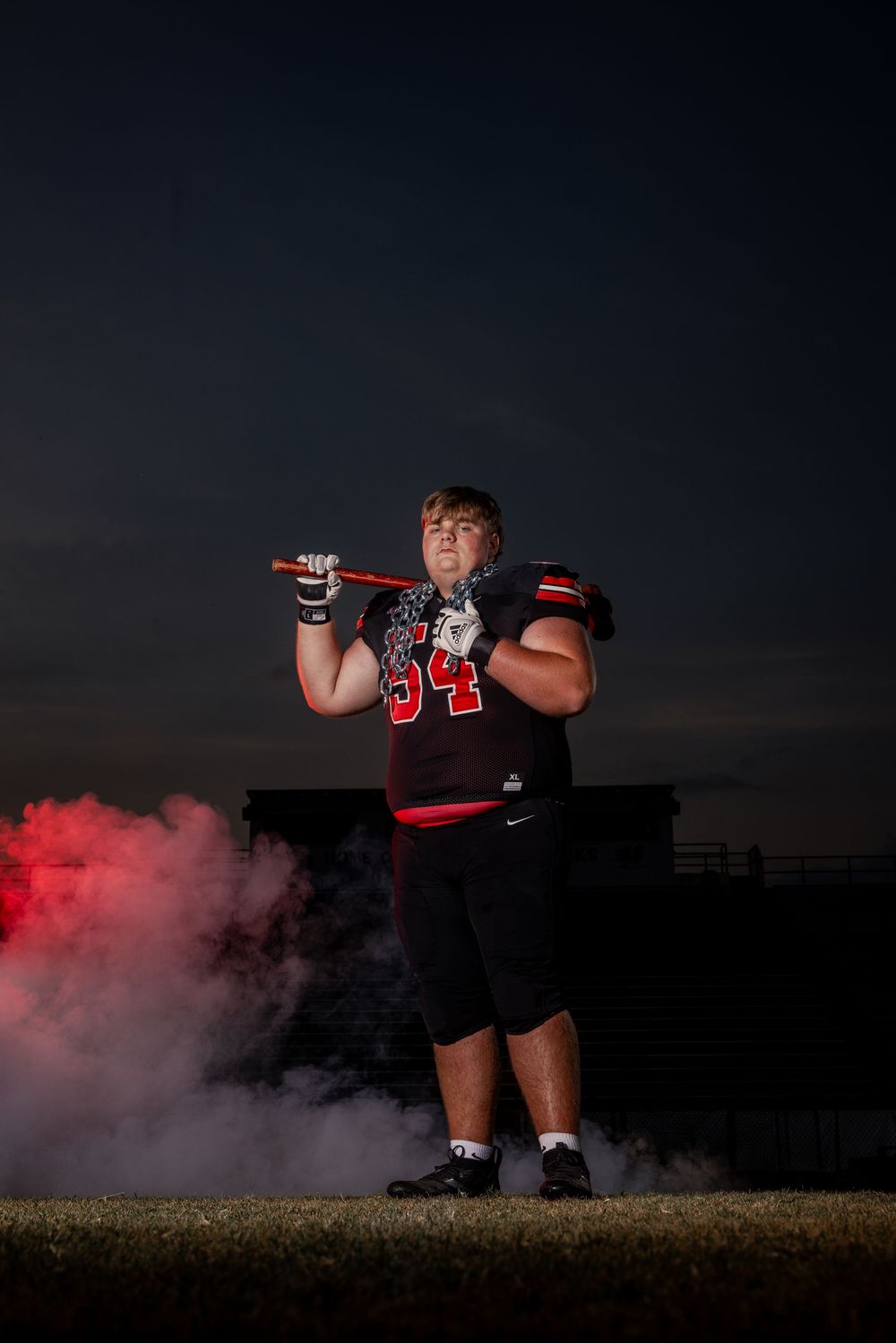 High school football player in jersey number 34 stands on field at night with red smoke effects.