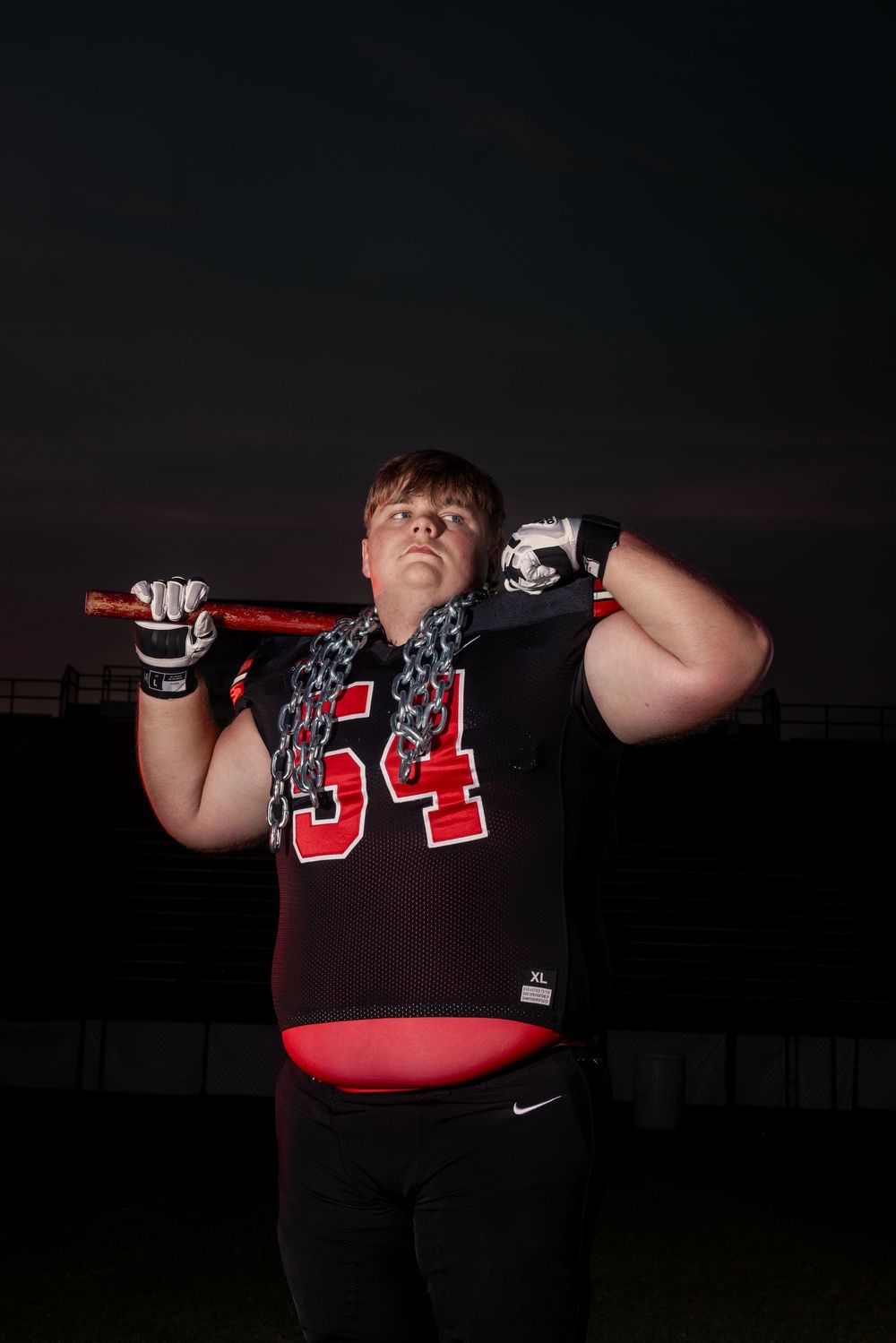 Football player in red and black jersey number 34 poses with equipment against dark evening sky.