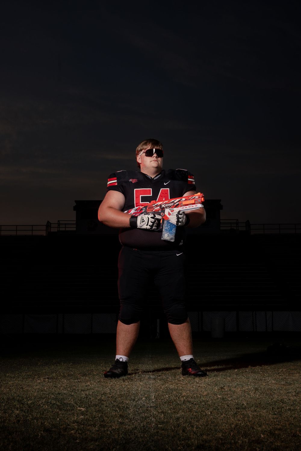 Football player in black uniform with number 54 poses dramatically at night on a dark field.