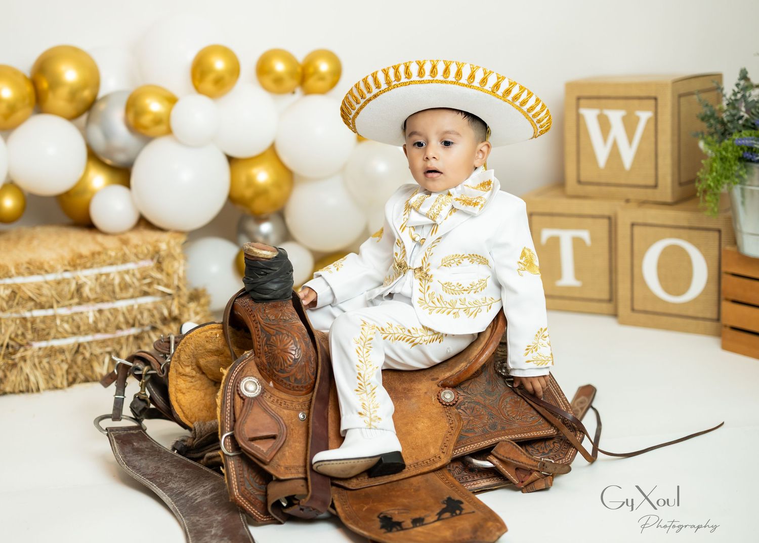 Brown rocking horse toy with gold and white balloon decorations and letter blocks in an elegant nursery setting.