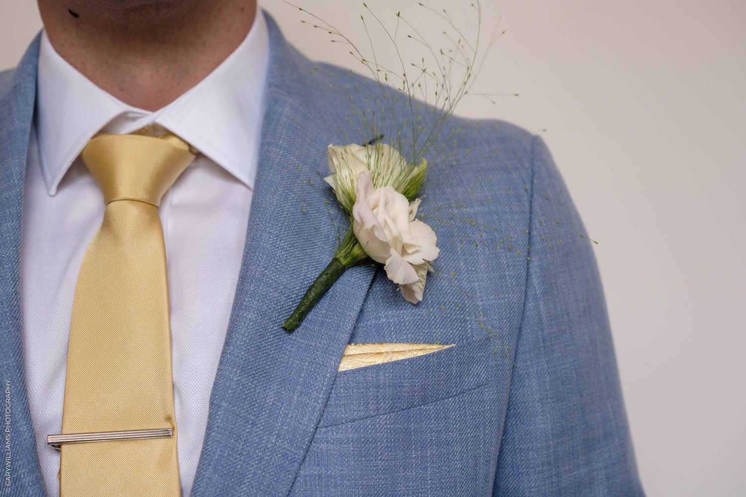 Close-up detail of a light blue suit jacket with yellow tie and white boutonniere flower.
