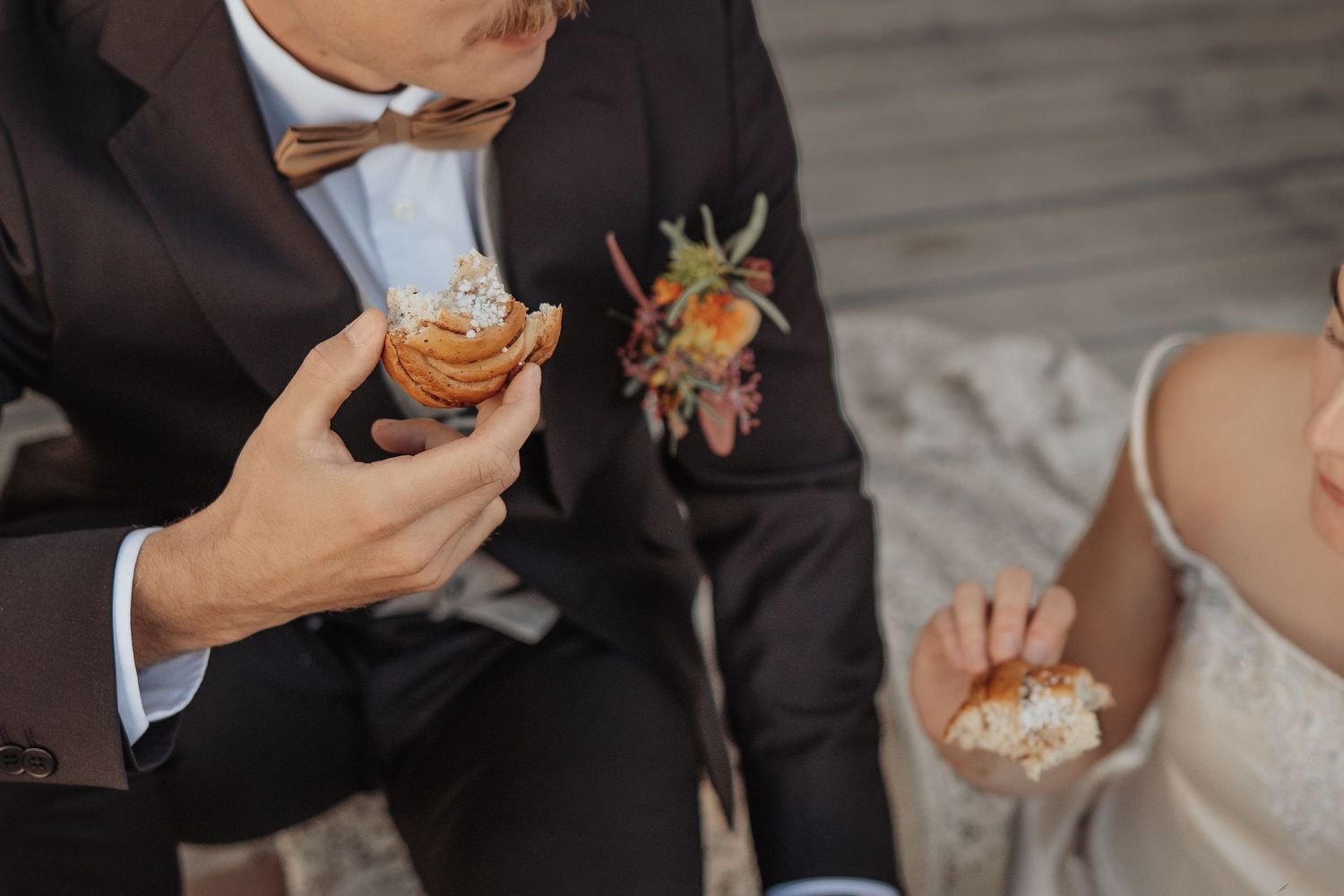 Bride and groom sharing cupcakes on their wedding day, groom wearing a suit with floral boutonniere.