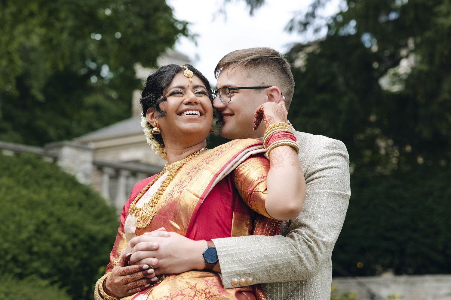 A couple shares intimate moments while exploring an outdoor garden in traditional Indian wedding attire.