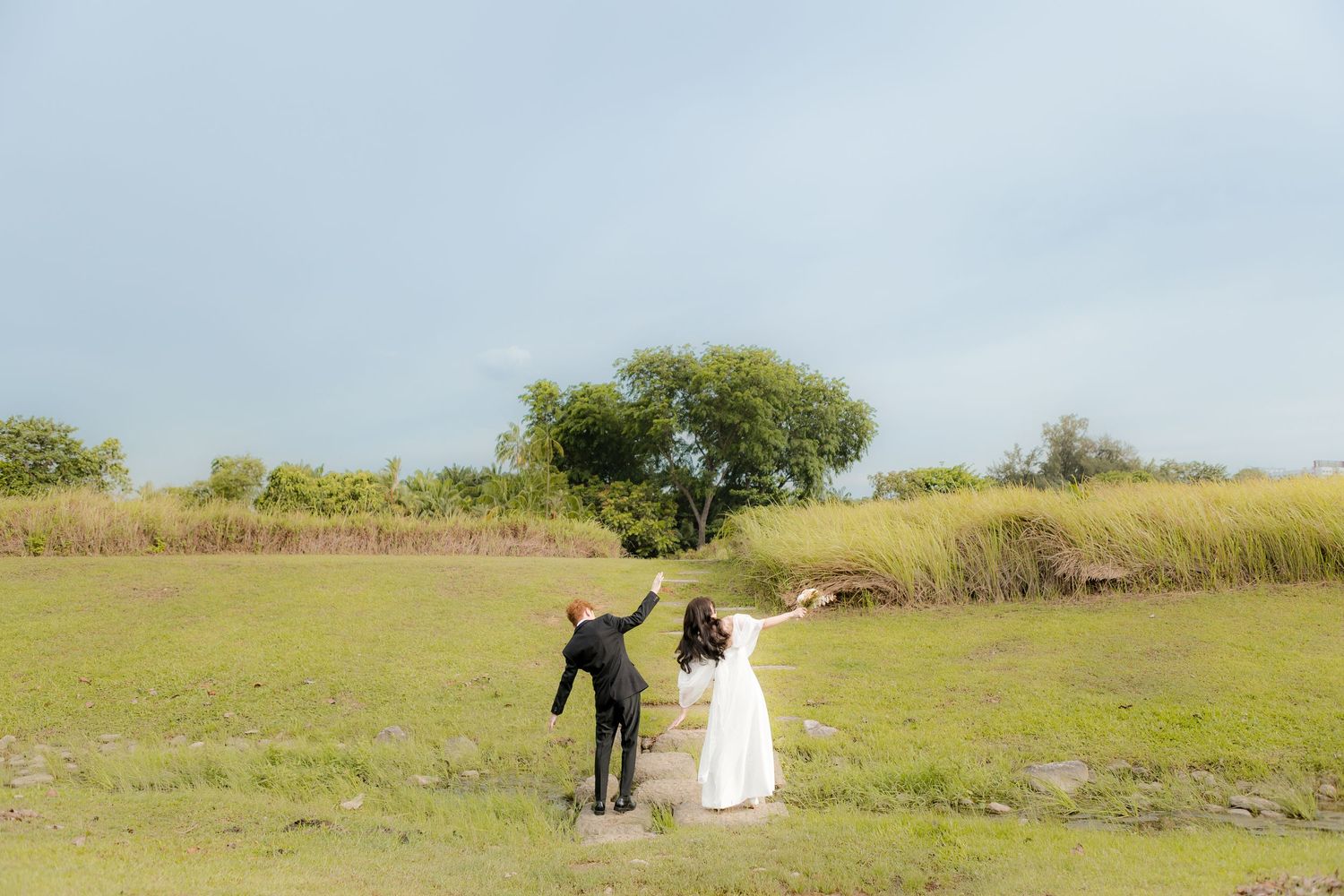 wedding couple in white dress and black suit. in a green grassy field with blue skies and lush long grass
