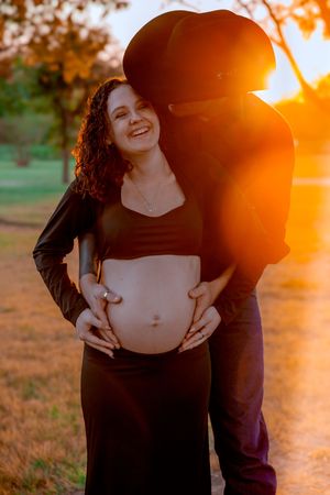 Maternity photoshoot at sunset in a field with warm golden light creating a romantic silhouette.