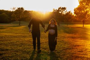Silhouetted couple walking together at sunset in a grassy field.