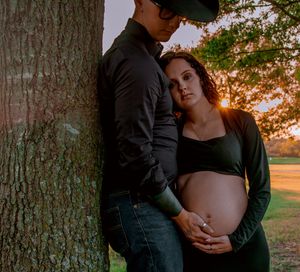 Intimate maternity photos taken near a large tree trunk during golden hour.