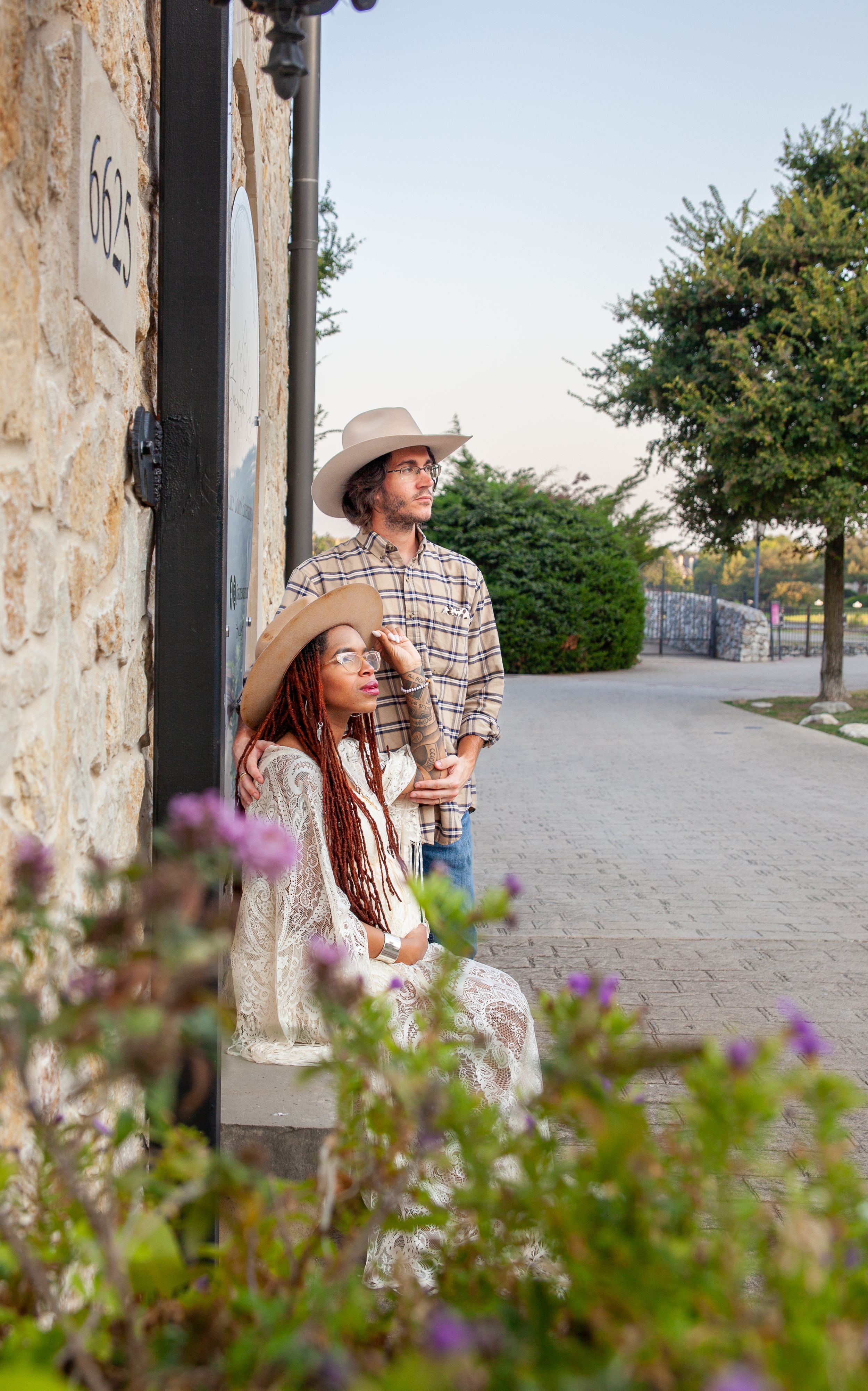 A couple relaxes in a rustic stone archway with purple wildflowers in the foreground.