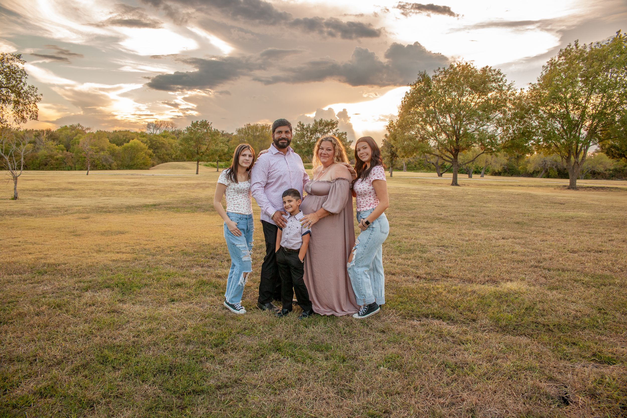 A family portrait session in a golden field during sunset with trees in the background.