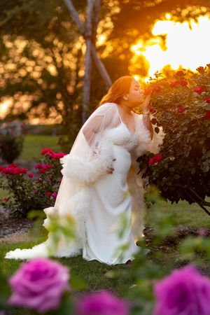White dress flowing in a garden with pink roses at sunset.