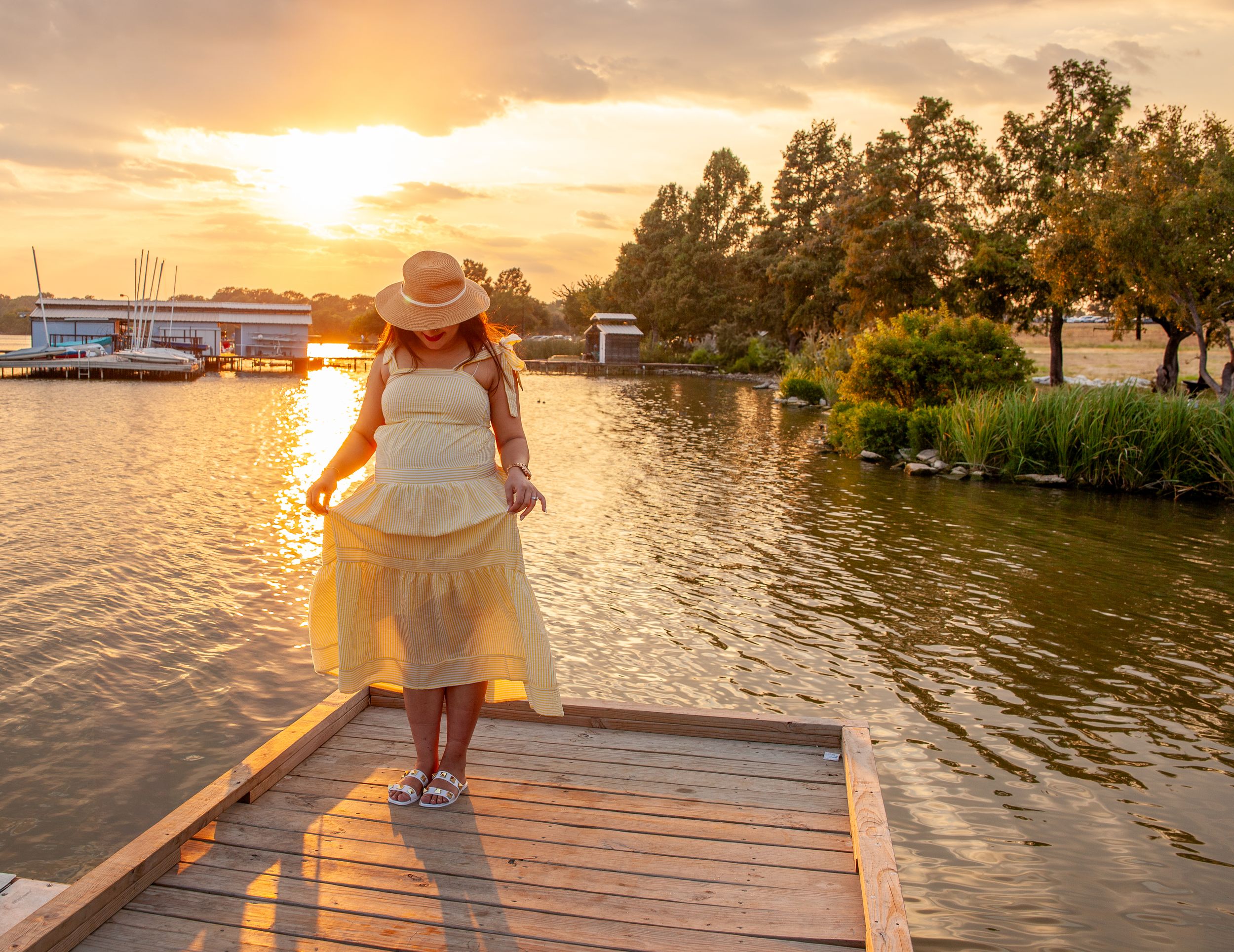 A person walks on a wooden dock at sunset overlooking a peaceful lake.