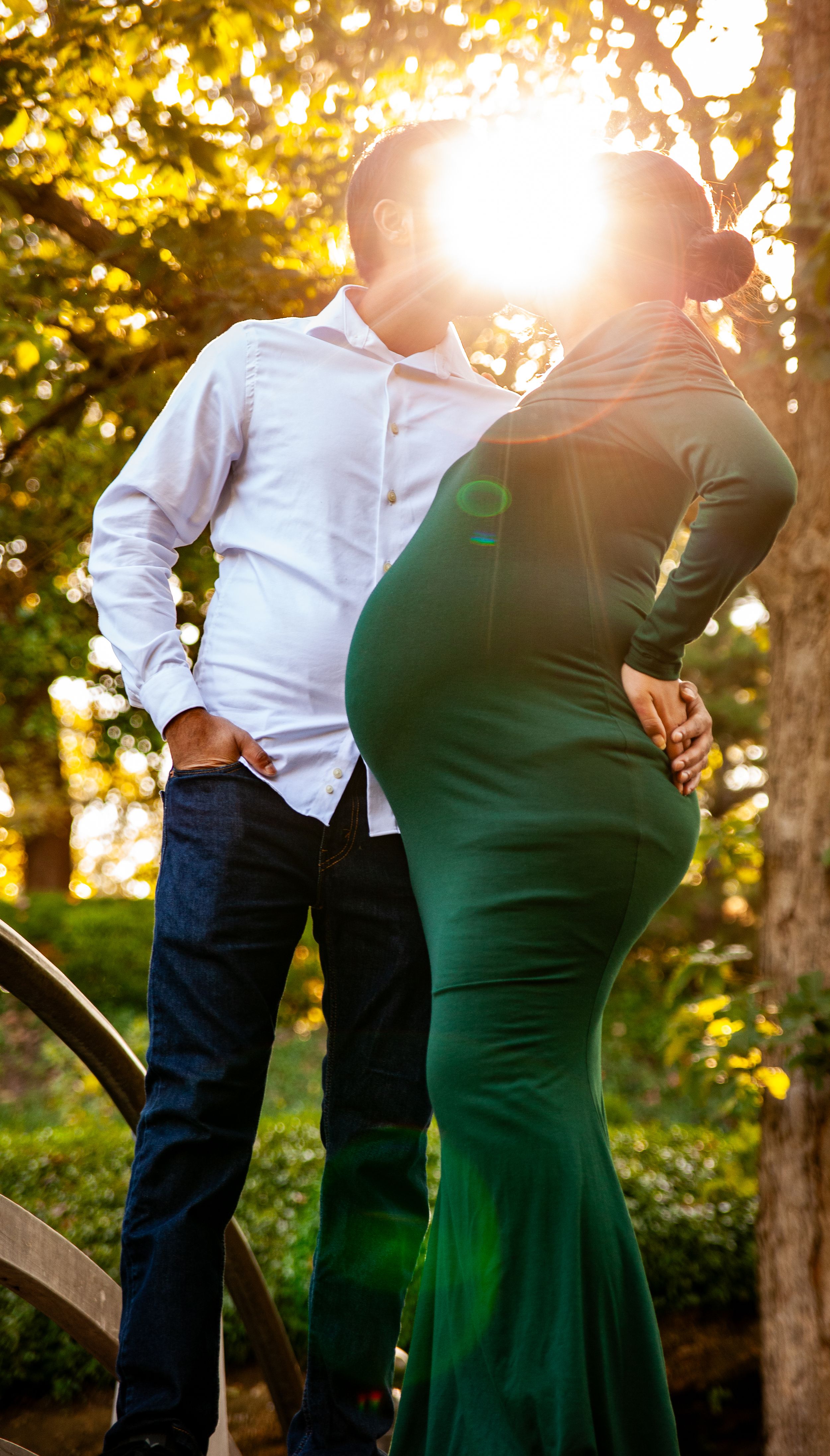 A backlit couple embracing on a wooden bridge during sunset.